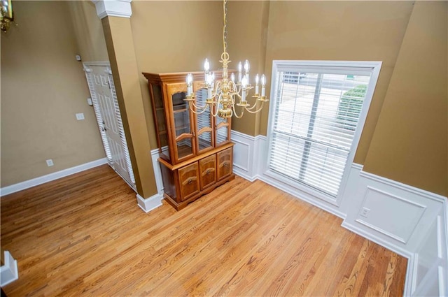 unfurnished dining area featuring wainscoting, light wood-style floors, and an inviting chandelier