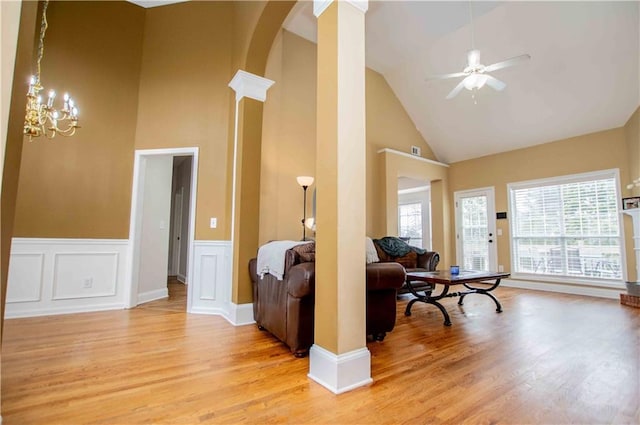 living room featuring a wealth of natural light, light wood-style flooring, ceiling fan with notable chandelier, and decorative columns