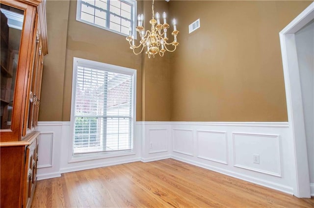 unfurnished dining area with an inviting chandelier, light wood-style floors, visible vents, and wainscoting