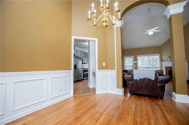 interior space with a wainscoted wall, a fireplace, arched walkways, ceiling fan, and light wood-style floors