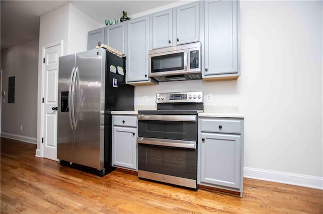 kitchen featuring light countertops, baseboards, light wood finished floors, and stainless steel appliances