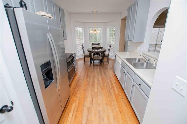 kitchen with light wood-type flooring, a sink, stainless steel fridge with ice dispenser, light countertops, and hanging light fixtures