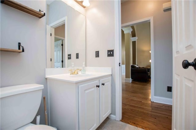 half bath with toilet, vanity, baseboards, and wood finished floors