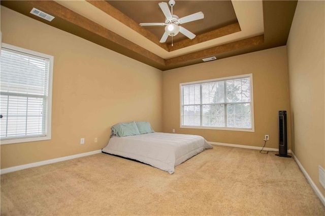 bedroom with a tray ceiling, multiple windows, and visible vents