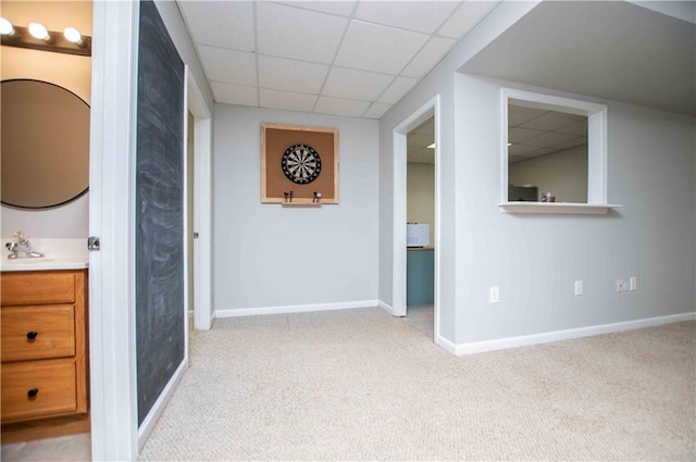 corridor featuring carpet flooring, a sink, baseboards, and a drop ceiling