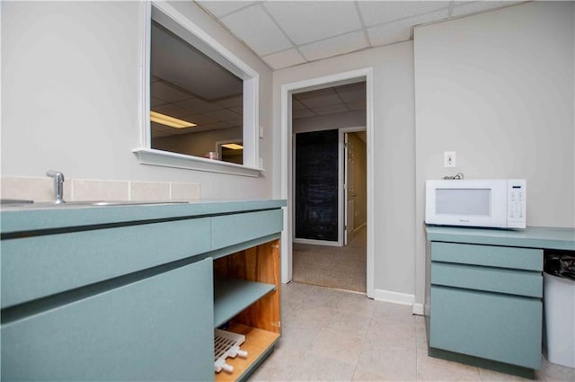 interior space featuring white microwave, light tile patterned floors, a paneled ceiling, and baseboards