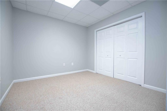 unfurnished bedroom featuring a closet, a drop ceiling, baseboards, and carpet floors