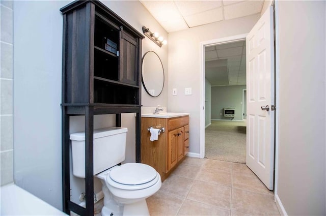 bathroom with tile patterned floors, toilet, a drop ceiling, heating unit, and vanity