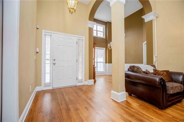 entrance foyer featuring arched walkways, a high ceiling, light wood-style floors, and ornate columns