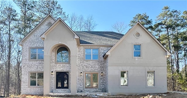 view of front of property with french doors, brick siding, and roof with shingles