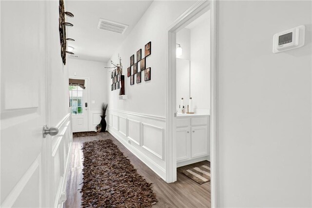 hallway featuring wood finished floors, wainscoting, and a decorative wall