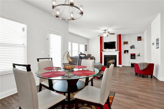 dining space featuring wood finished floors, a chandelier, a ceiling fan, baseboards, and a glass covered fireplace