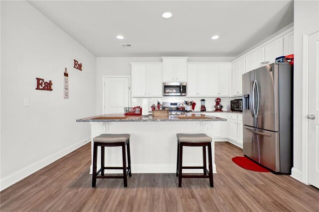 kitchen featuring stainless steel appliances, a kitchen bar, wood finished floors, white cabinetry, and recessed lighting