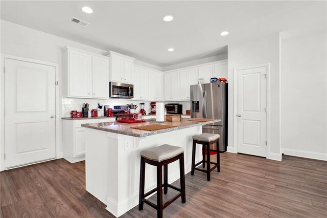 kitchen featuring appliances with stainless steel finishes, a kitchen bar, dark wood-style flooring, a center island, and recessed lighting