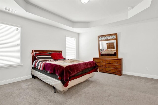 bedroom with a tray ceiling, carpet floors, and baseboards