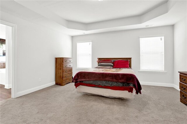 bedroom with carpet, a raised ceiling, and baseboards