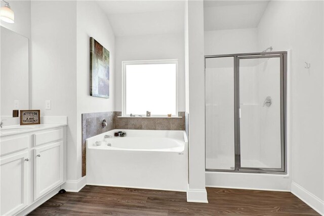 bathroom featuring wood finished floors, a stall shower, a garden tub, vanity, and baseboards