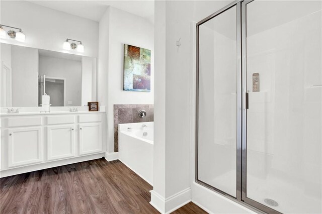 full bath featuring a bath, wood finished floors, a shower stall, double vanity, and baseboards
