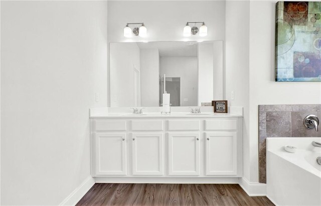 full bath featuring wood finished floors, a garden tub, baseboards, and double vanity