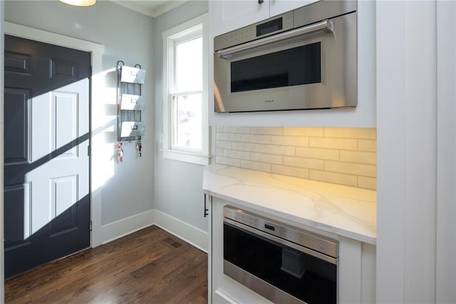 kitchen featuring decorative backsplash, dark wood finished floors, white cabinets, appliances with stainless steel finishes, and light stone counters