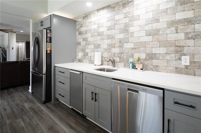 kitchen featuring decorative backsplash, appliances with stainless steel finishes, dark wood-type flooring, gray cabinetry, and a sink