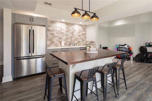 kitchen with a raised ceiling, appliances with stainless steel finishes, dark wood-style flooring, gray cabinets, and backsplash