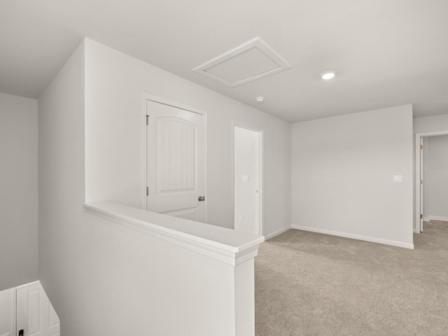 spare room featuring attic access, light carpet, and baseboards