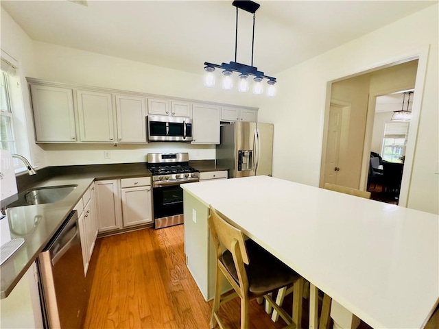 365 Friars Head Dr, Suwanee, GA 30024 - kitchen featuring appliances with stainless steel finishes, a sink, light wood finished floors, decorative light fixtures, and dark countertops