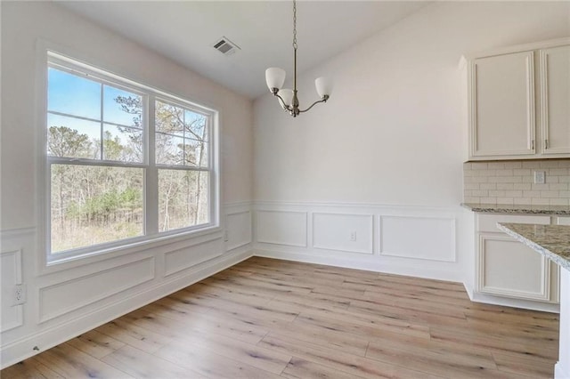 unfurnished dining area with an inviting chandelier, light hardwood / wood-style floors, and lofted ceiling