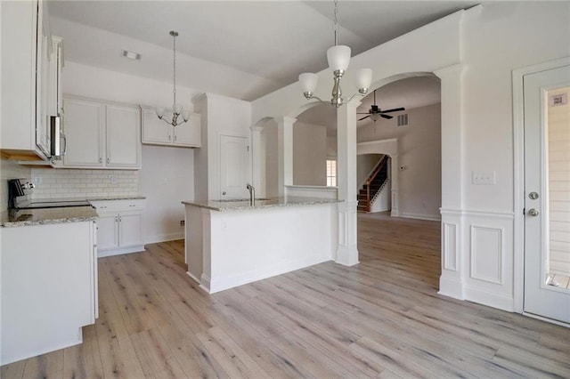 kitchen with decorative light fixtures, white cabinets, backsplash, stainless steel appliances, and a center island with sink