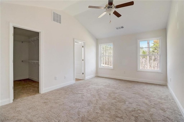 unfurnished bedroom featuring vaulted ceiling, a walk in closet, light carpet, and ceiling fan