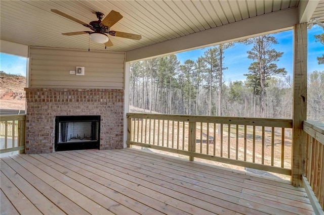 wooden deck with an outdoor brick fireplace and ceiling fan