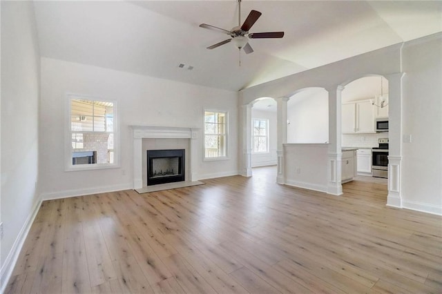 unfurnished living room with ornate columns, ceiling fan, vaulted ceiling, and light wood-type flooring