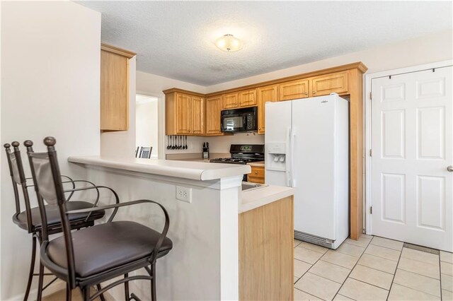 kitchen with a breakfast bar, black appliances, light tile patterned floors, a textured ceiling, and kitchen peninsula