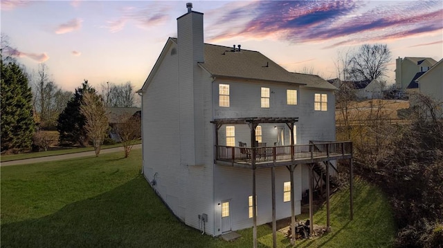 back house at dusk featuring a pergola, a wooden deck, and a lawn