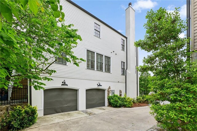 view of property exterior with a garage, stucco siding, driveway, and a chimney