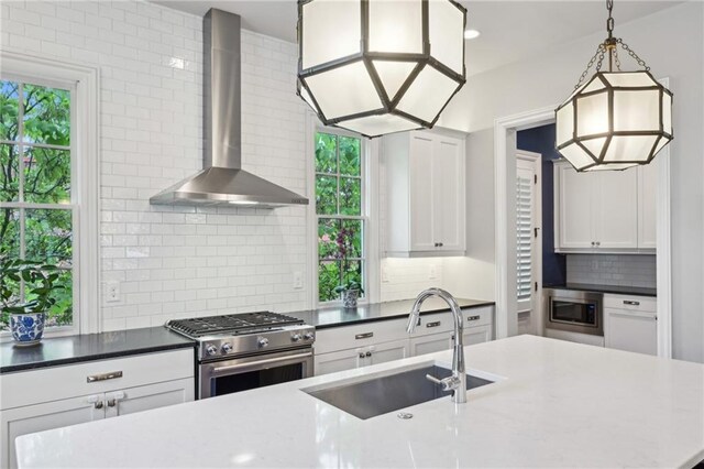 kitchen featuring wall chimney range hood, white cabinets, a sink, stainless steel appliances, and tasteful backsplash
