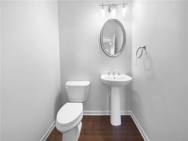 half bath featuring toilet, a sink, baseboards, and wood finished floors