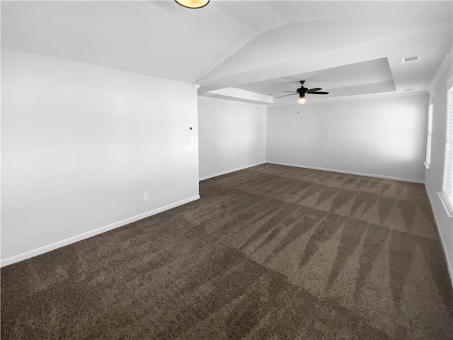 carpeted empty room featuring baseboards, vaulted ceiling, visible vents, and a raised ceiling
