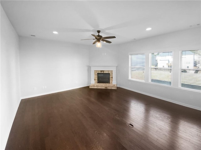 unfurnished living room featuring a brick fireplace, baseboards, and dark wood-style floors