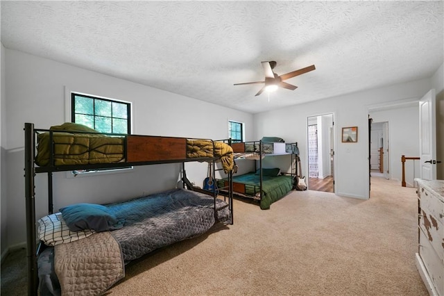 bedroom featuring ceiling fan, multiple windows, a textured ceiling, and light carpet