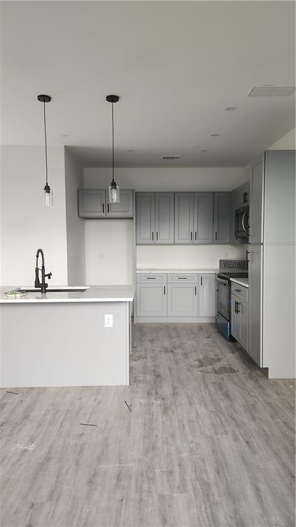 kitchen with black range with electric cooktop, light wood-style floors, gray cabinets, a sink, and decorative light fixtures