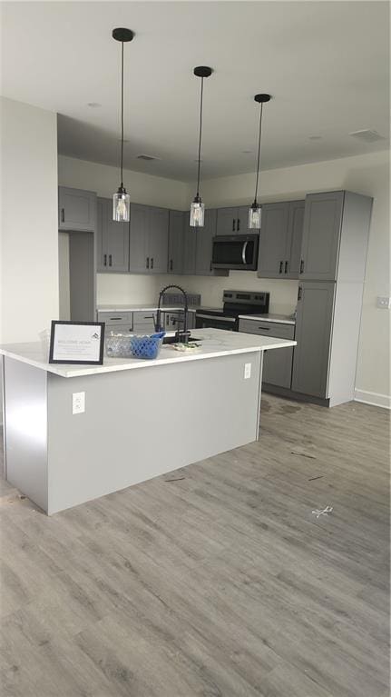 kitchen with appliances with stainless steel finishes, gray cabinetry, a sink, and light wood finished floors