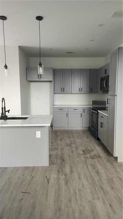 kitchen with range with electric stovetop, a sink, gray cabinets, and light wood-style flooring
