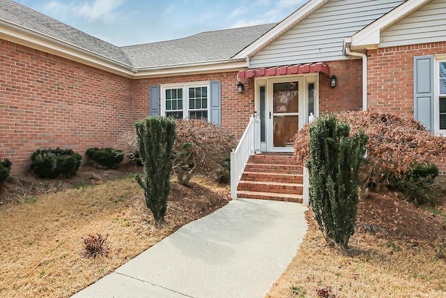 property entrance with a shingled roof and brick siding