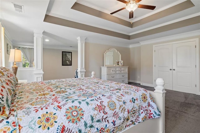 carpeted bedroom featuring ceiling fan, ornate columns, ornamental molding, a tray ceiling, and a closet