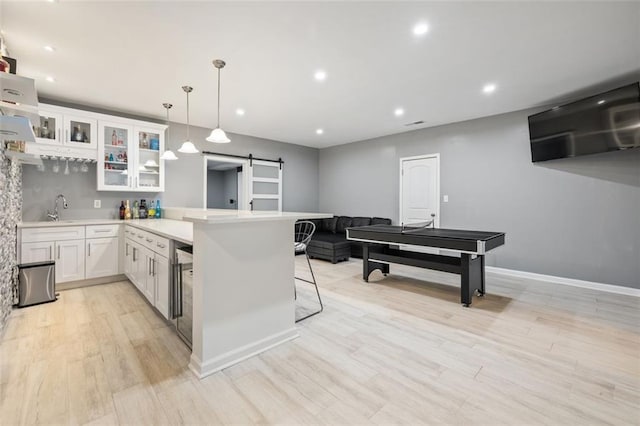 kitchen featuring kitchen peninsula, a kitchen breakfast bar, a barn door, white cabinets, and hanging light fixtures