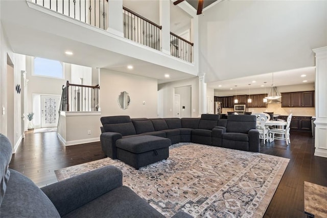 living room with ceiling fan, dark hardwood / wood-style flooring, and a towering ceiling