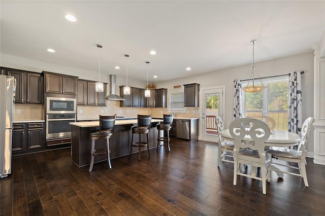 kitchen featuring hanging light fixtures, wall chimney exhaust hood, dark hardwood / wood-style floors, a kitchen island, and stainless steel appliances