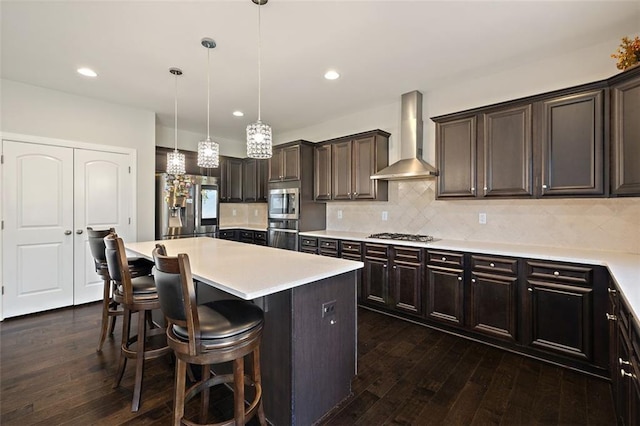 kitchen featuring stainless steel appliances, wall chimney range hood, decorative light fixtures, a center island, and dark hardwood / wood-style floors